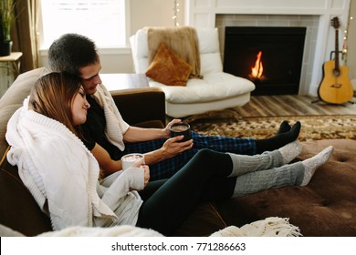 Couple cuddling on the couch drinking hot chocolate in front of fire