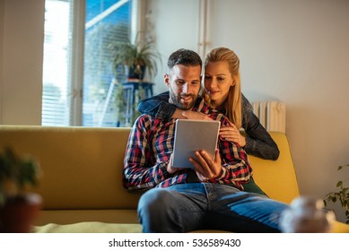 Couple Cuddling And Watching Series Online On A Tablet.