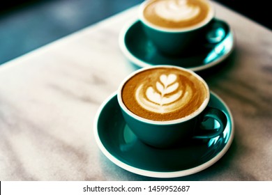 A couple cups of cappuccino art coffee with foam in the shape of a tulip on a marble background, place for text