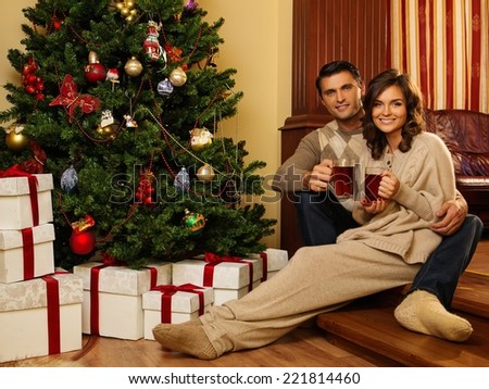 Couple with cups of hot drink near Christmas tree