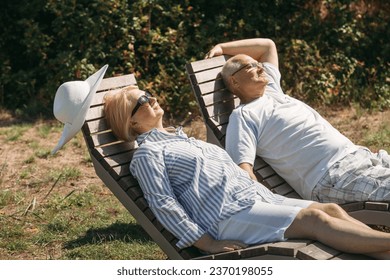 A couple of cute elderly people lie on sunbeds holding hands, basking in the sun. - Powered by Shutterstock