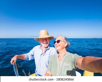 couple of cute mature people or senior enjoying and having fun together in the middle of the sea or ocean with a small boat or dinghy - woman pensioner taking a selfie with her old man driving the boat - Powered by Shutterstock