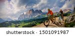 Couple cycling on electric bike, rides mountain trail. Woman and Man riding on bikes in Dolomites mountains landscape. Cycling e-mtb enduro trail track. Outdoor sport activity.