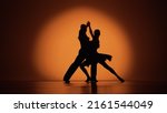 Couple of dancers approach each other and begin to dance Argentine tango. Elements of latin ballroom dance in studio with orange brown background. Dark silhouettes. Slow motion ready, 4K at 59.94fps.