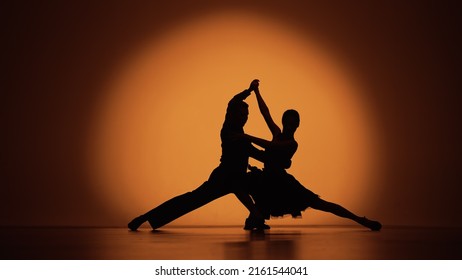 Couple Of Dancers Approach Each Other And Begin To Dance Argentine Tango. Elements Of Latin Ballroom Dance In Studio With Orange Brown Background. Dark Silhouettes. Slow Motion Ready, 4K At 59.94fps.