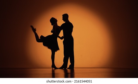 Couple Of Dancers Approach Each Other And Begin To Dance Argentine Tango. Elements Of Latin Ballroom Dance In Studio With Orange Brown Background. Dark Silhouettes. Slow Motion Ready, 4K At 59.94fps.