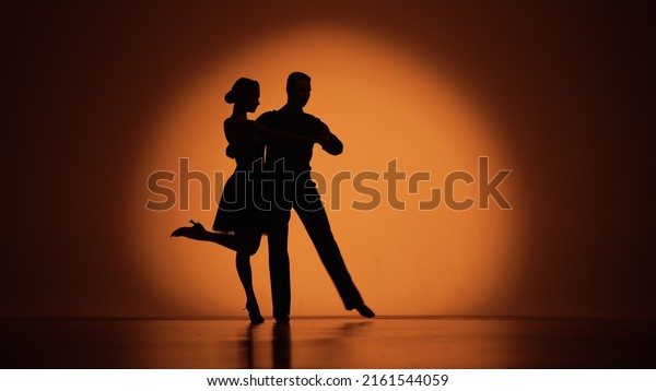 Couple of dancers approach each other and begin\
to dance Argentine tango. Elements of latin ballroom dance in\
studio with orange brown background. Dark silhouettes. Slow motion\
ready, 4K at 59.94fps.