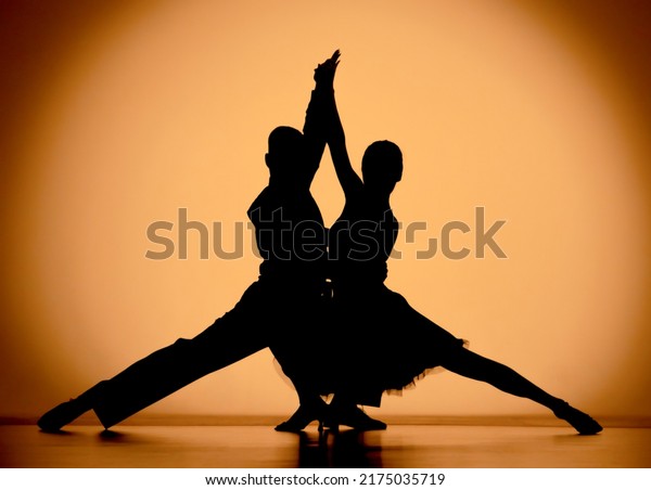 Couple of dancers are dancing elements of\
Argentine tango. Black silhouettes of man and woman on an orange\
brown gradient background in studio. Screensaver for school of\
ballroom Latin American\
dances