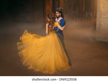 couple is dancing at fantasy ball. Happy beauty woman princess in yellow dress and guy enchanted guy, horns on head. Girl whirls in arms of male prince. Man monster costume. Silk fabric fly in motion