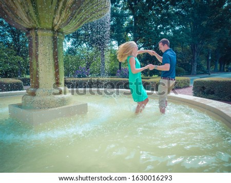 A couple dancing in a fountain in a park surrounded by greenery under sunlight