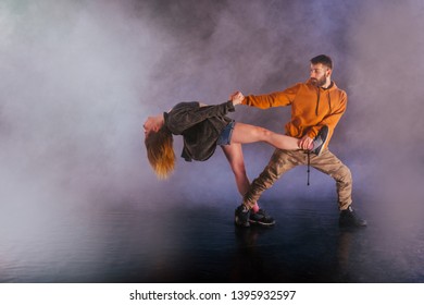 Couple dancing modern dance and showing off their leg stretch moves.Black background while the couple is dressed in urban colorful clothes. - Powered by Shutterstock