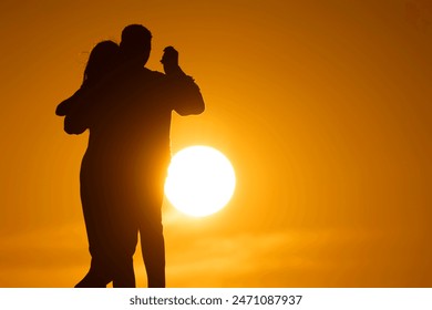 A couple is dancing in the sun, with the sun in the background