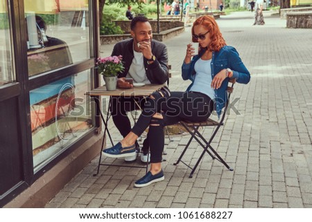 A couple dating drinking coffee, sitting near the coffee shop. Outdoors on a date.