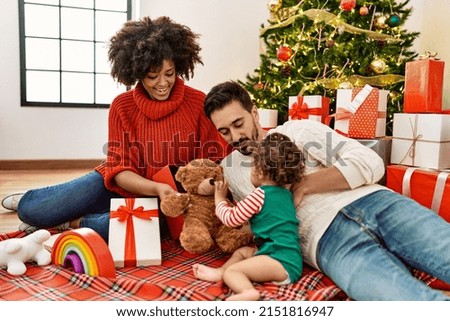 Couple and daughter playing with toys sitting by christmas tree at home