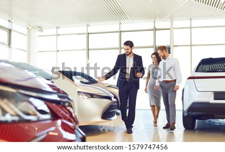 Couple and the dealer selling cars look the car in the showroom.