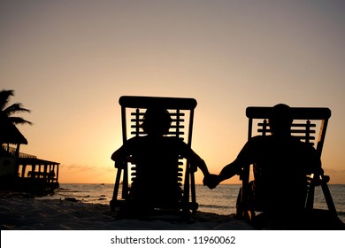 Couple in deckchairs holding hands at sunset