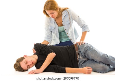 Couple Demonstrating First Aid Techniques With Male Patient Lying In Recovery Position And Female Sitting Above Him.