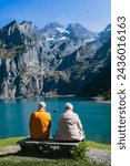 Couple âgé devant le lac Oeschinensee en Suisse (Oshinen Lake, Switzerland), montagnes suisses, barque, calme.