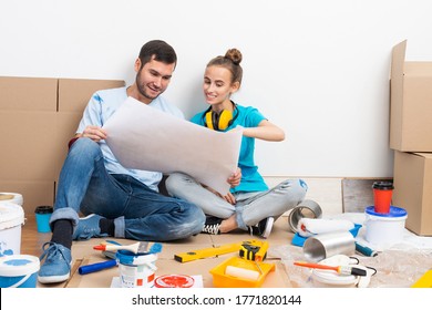 Couple Discussing Home Redesign Ideas. Man And Woman Together Planning New Home Interior Design. Cardboard Boxes, Painting Tools And Materials On Floor. House Remodeling And Architectural Renovation.