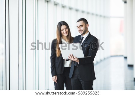 Couple discussing new project on the laptop atanding against in office room with panoramic windows