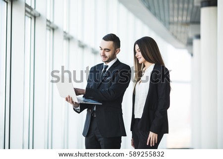 Couple discussing new project on the laptop atanding against in office room with panoramic windows