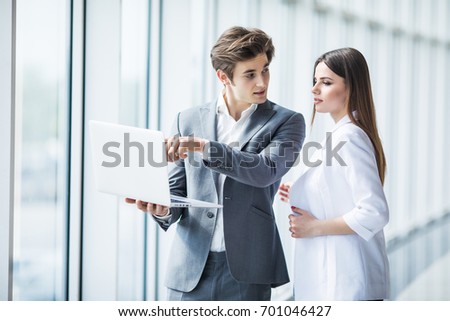 Couple discussing new project on the laptop standing against in office room with panoramic windows