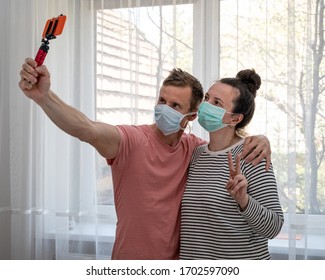 Couple In Disposable Masks Taking Selfie At Home. Social Distancing