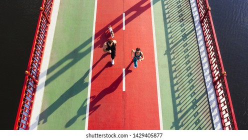 Couple With Dog Running Marathon On Green And Red Bridge. Time For Sport. Healthy Vibes Lifestyle. Aerial Drone Top View