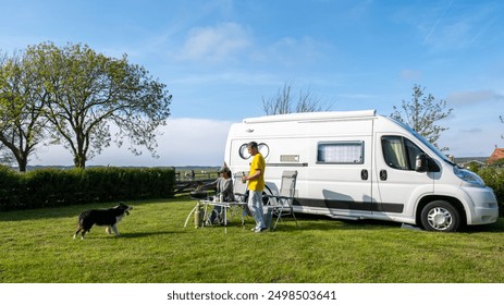 a couple with a dog are seated in front of their RV or camper van, enjoying the surroundings of a grassy field in Texel, Netherlands. a couple of man and woman camping at a farm in Texel Netherlands - Powered by Shutterstock