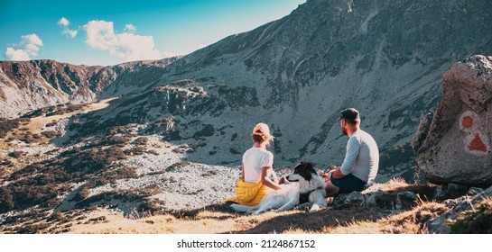 couple with dog sitting on rocks admiring mountain landscape
