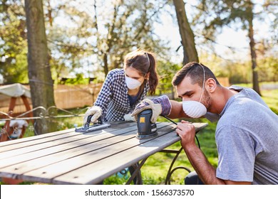 Couple Doing Home Improvement In The Garden With Grinder While Grinding Off A Wooden Table