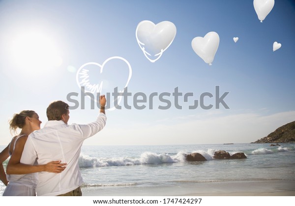 Couple drawing\
digital hearts in sky at\
beach