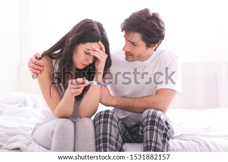 Couple dreaming to be parents. Upset man comforting his depressed wife with negative pregnancy test, free space