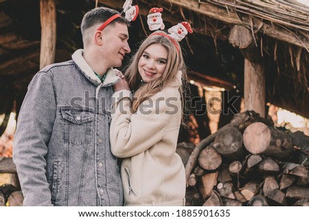 
A couple dressed in New Year's hoops on their heads are smiling at each other against the background of a gazebo made of firewood