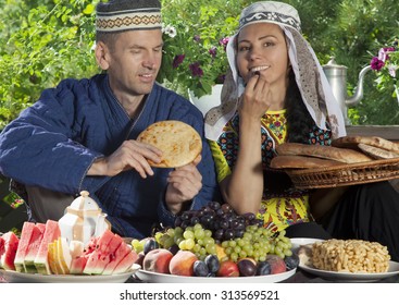 Couple dressed in Uzbekistan clothes have breakfast with fruits and flat cake