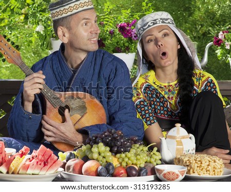 Couple dressed in Uzbekistan clothes playing mandolin and singing during breakfast
