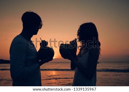 Couple drinking cocnut juice while watching the sunset over the ocean in Bali, Indonesia.