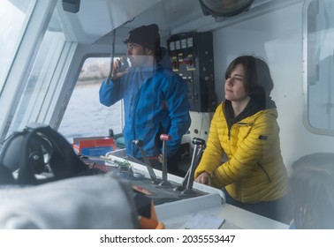 Couple driving a boat from the cabin while talking on the radio.
