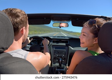 Couple Driving Car On Road Trip Travel Vacation In Convertible. Young Romantic Couple On Travel Holidays Vacation. Man Driver Behind Steering Wheel.