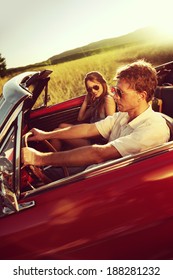 Couple Driving Convertible Car Enjoying A Summer Day At Sunset