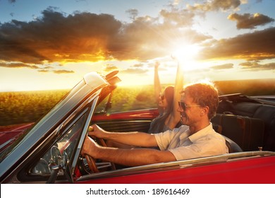 Couple Driving Convertible Car Enjoying A Summer Day At Sunset