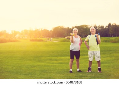 Couple with dumbbells smiling. Senior people standing outdoor. New training program for pensioners. Life and sports. - Powered by Shutterstock