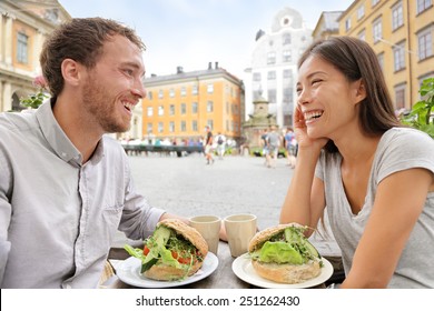 Couple eating food at Cafe in Stockholm, Sweden, Europe. Happy multiracial young couple outside on Stortorget big square in Gamla Stan, the old town of Stockholm. Scandinavian man, Asian woman.