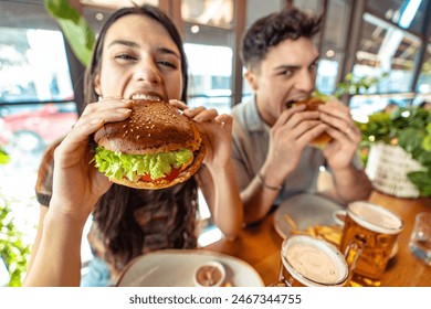 Couple eating fresh burger sitting at pub restaurant table  - Powered by Shutterstock