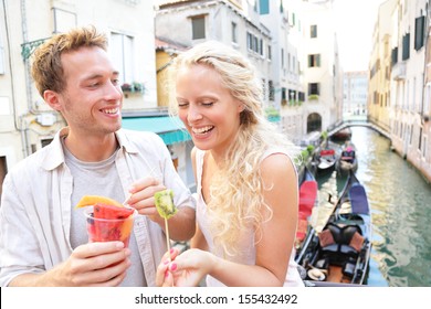 Couple Eating Fruit Snack In Venice. Lifestyle Image Of Beautiful Young Couple Eating Healthy Food On On Travel Vacation In Venice, Italy. Pretty Blonde Woman And Handsome Man In Their Twenties.