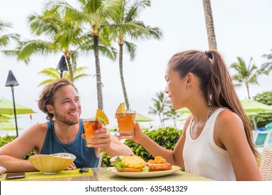 Couple Eating At Hotel Restaurant On Hawaii Travel Vacation Beach Drinking Hawaiian Drink Mai Tai. Happy People Toasting Cheers With Cocktails. Summer Holidays At Resort.