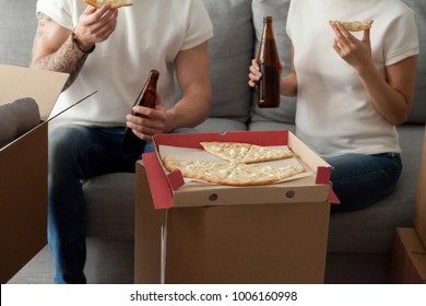 Couple eating pizza celebrating housewarming party on moving day, man and woman enjoying beer and snack sitting on sofa with unpacked boxes around, move in new home, delivery service, close up view - Powered by Shutterstock