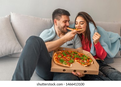 The Couple Eating A Pizza And Watch A Movie On The Sofa. Couple Sharing Pizza And Eating Together Happily. Couple Take A Break On Sofa With Pizza. Happy Couple Watching Tv 