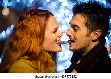 Couple eating together one piece of chocolate in street at night with christmas tree in background