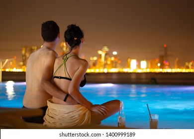 A Couple At The Edge Of Infinity Pool At The Happiness Island In Abu Dhabi, Distant City Light At Night 